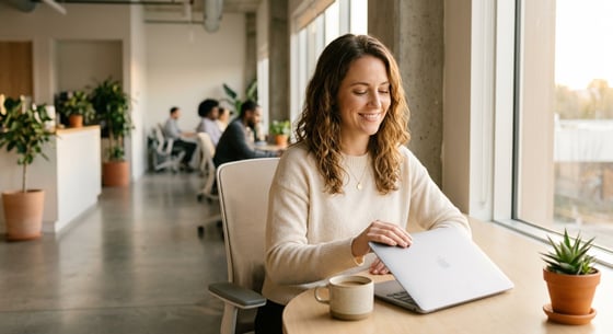 Mulher sorridente fechando o laptop em um espaço de coworking iluminado, representando o equilíbrio entre vida pessoal e profissional